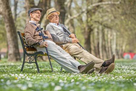 Due signori anziani rilassati su una panchina di legno in un parco primaverile – previdenza complementare e benessere nella terza età